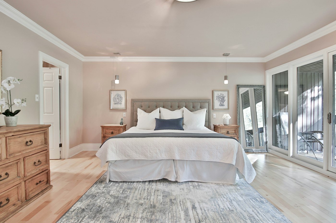 A bedroom with a white quilt, a grey headboard, wooden chests, and a pale rug