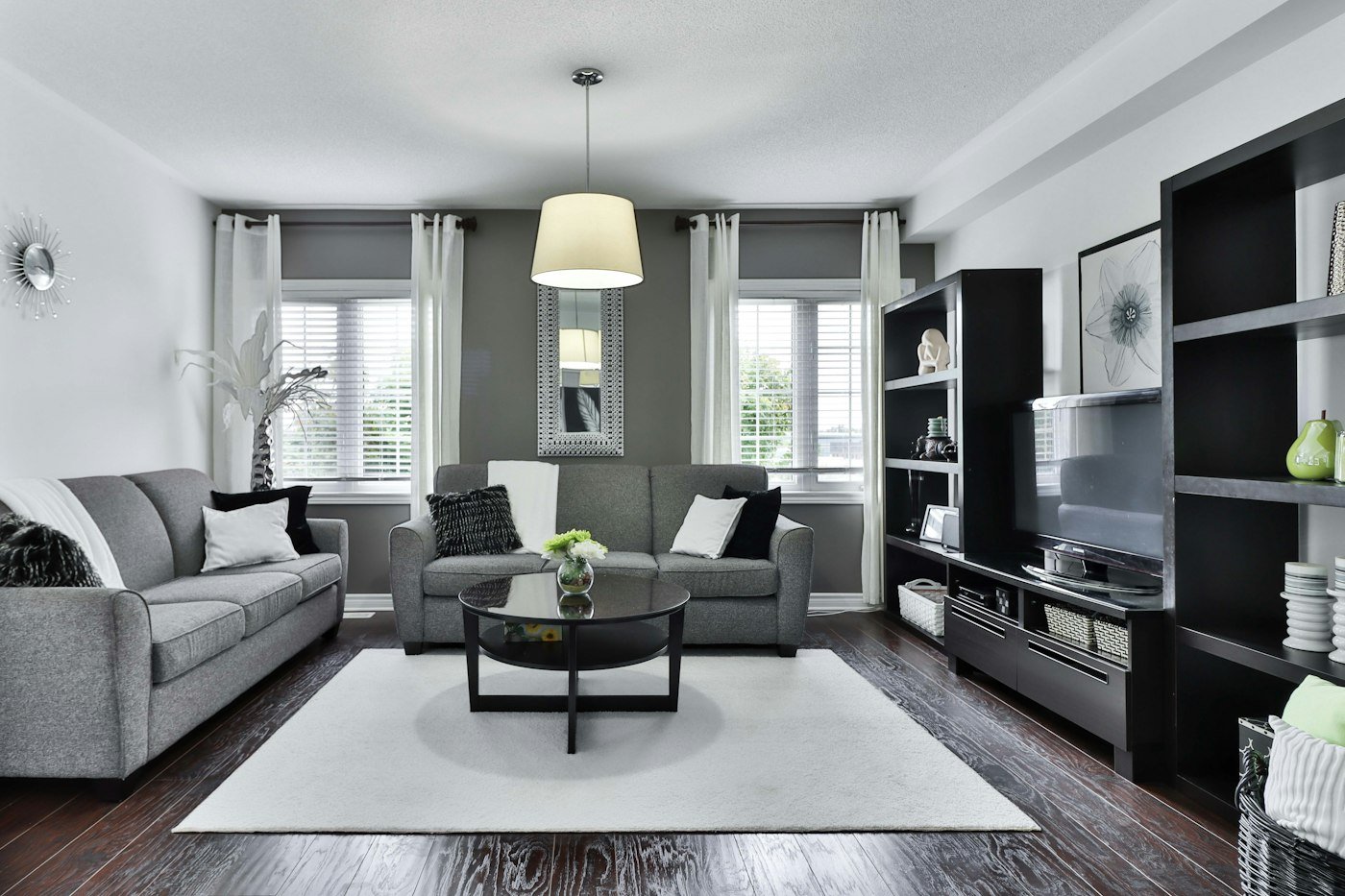A living room with two grey sofas, a round black table, a white rug, and a black shelving unit